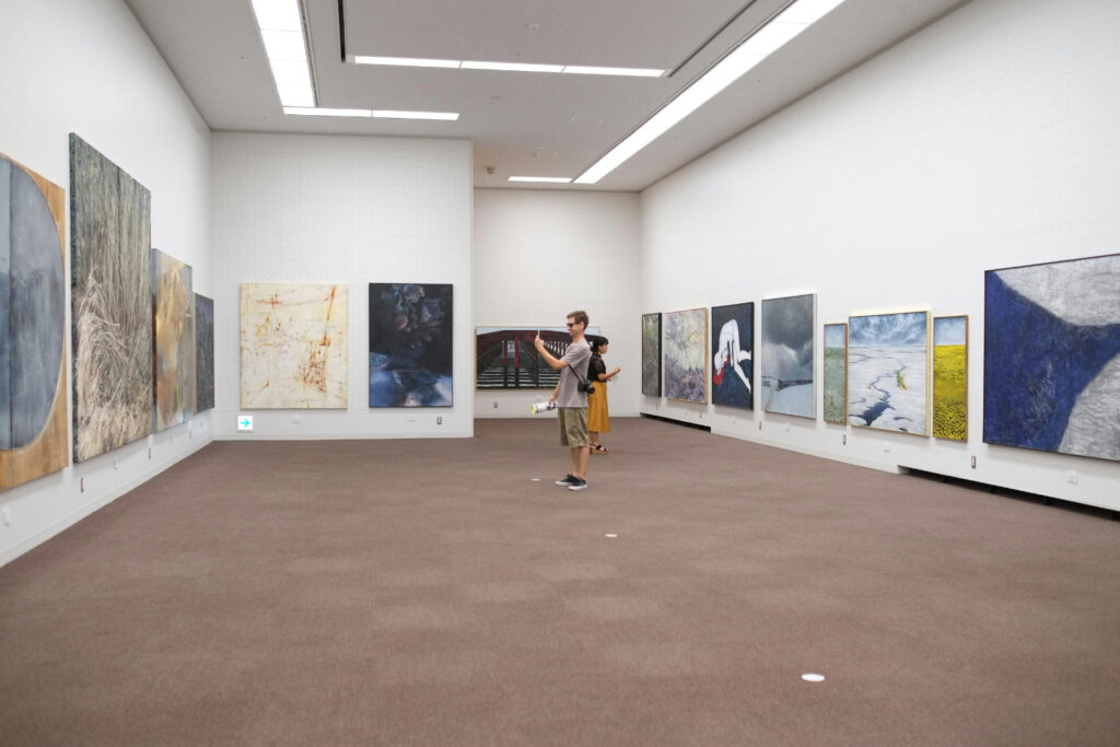 An image in a Tokyo gallery of two people enjoy art and culture. A large white room with large art around the outside walls.