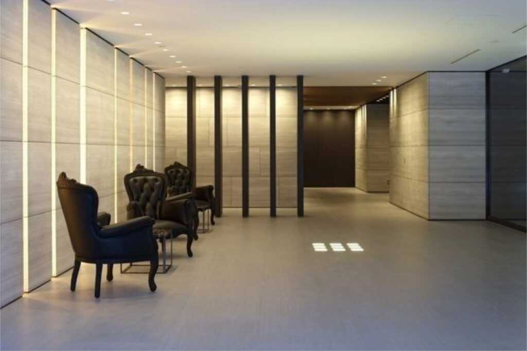 Seating area at The Westminster Roppongi lined with pale stone walls, vertical light strips and tufted leather chairs