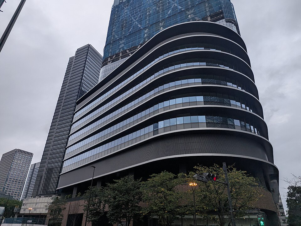 Torch Tower under construction in Tokiwabashi, its curved podium facade complete while the tower above remains clad in construction netting