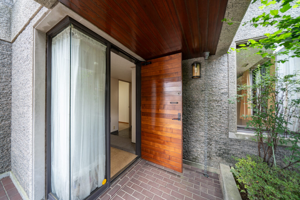 Timber front door and covered entrance porch of a detached house in central Tokyo, opening onto brick paving.