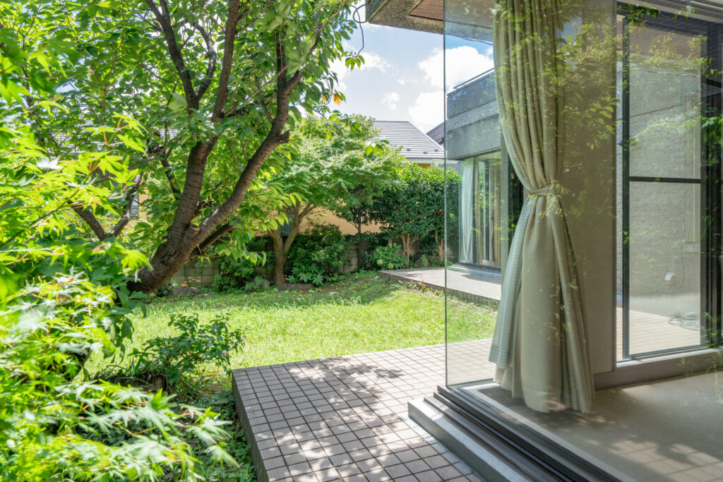 Private garden with lawn and mature maple and cherry trees, seen through full-height glass doors from inside the house.