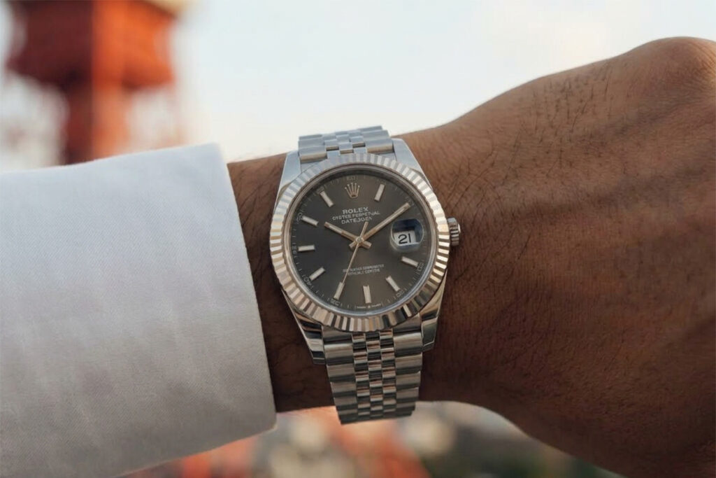 Rolex watch on a businessman's wrist with Tokyo Tower in the background. Silver bezel and strap, Black watch face.